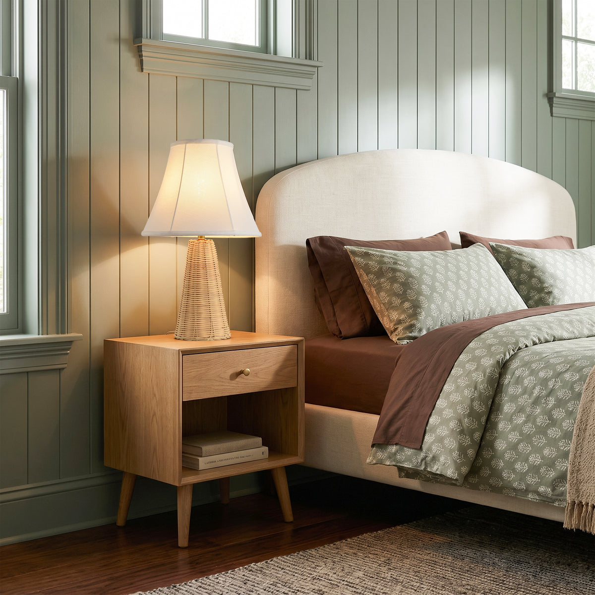 Modern bedroom with a wooden nightstand, woven lamp, and bed with neutral linens.
