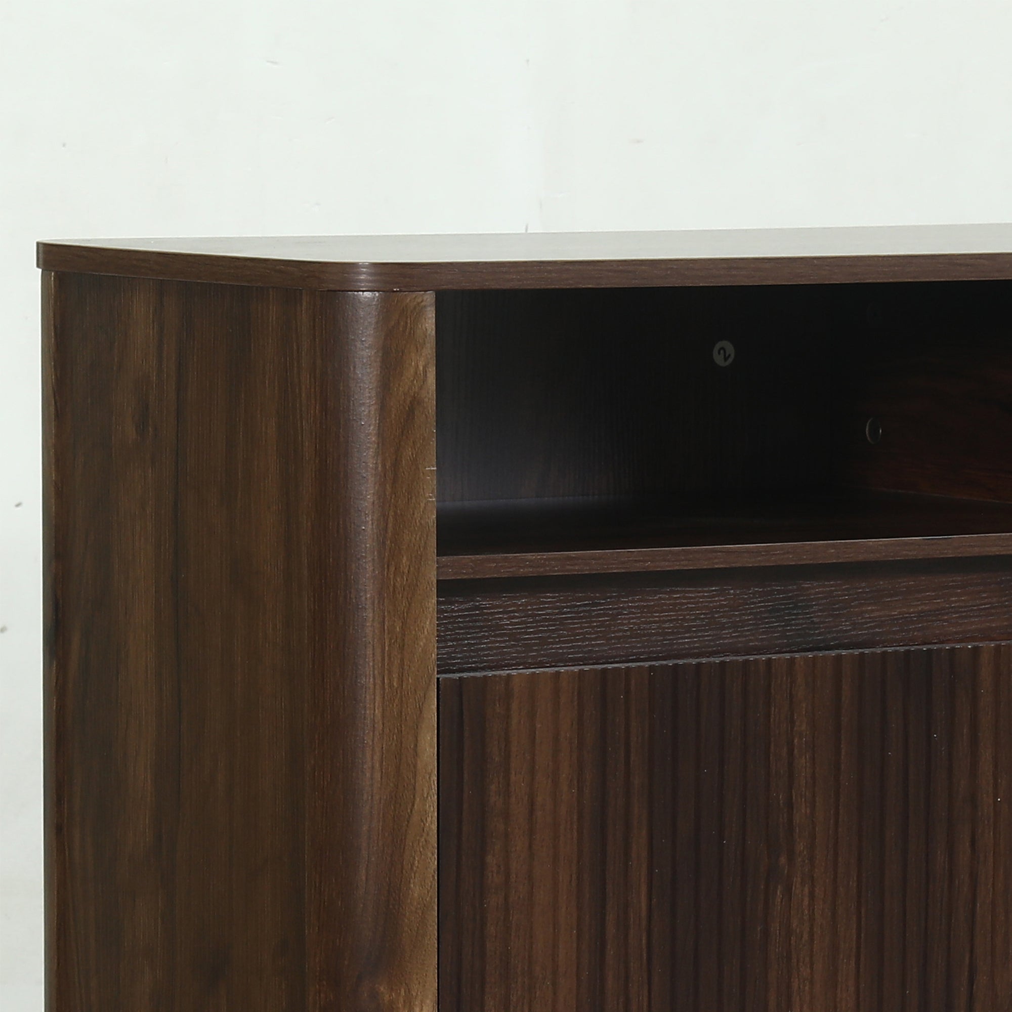 Close-up detail of a dark walnut wood furniture cabinet with a curved edge and open shelf.