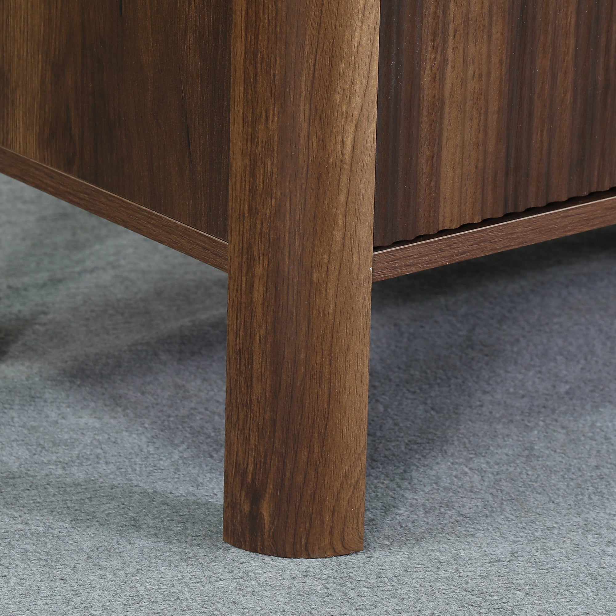 Close-up of a walnut wood furniture leg on a grey carpeted floor