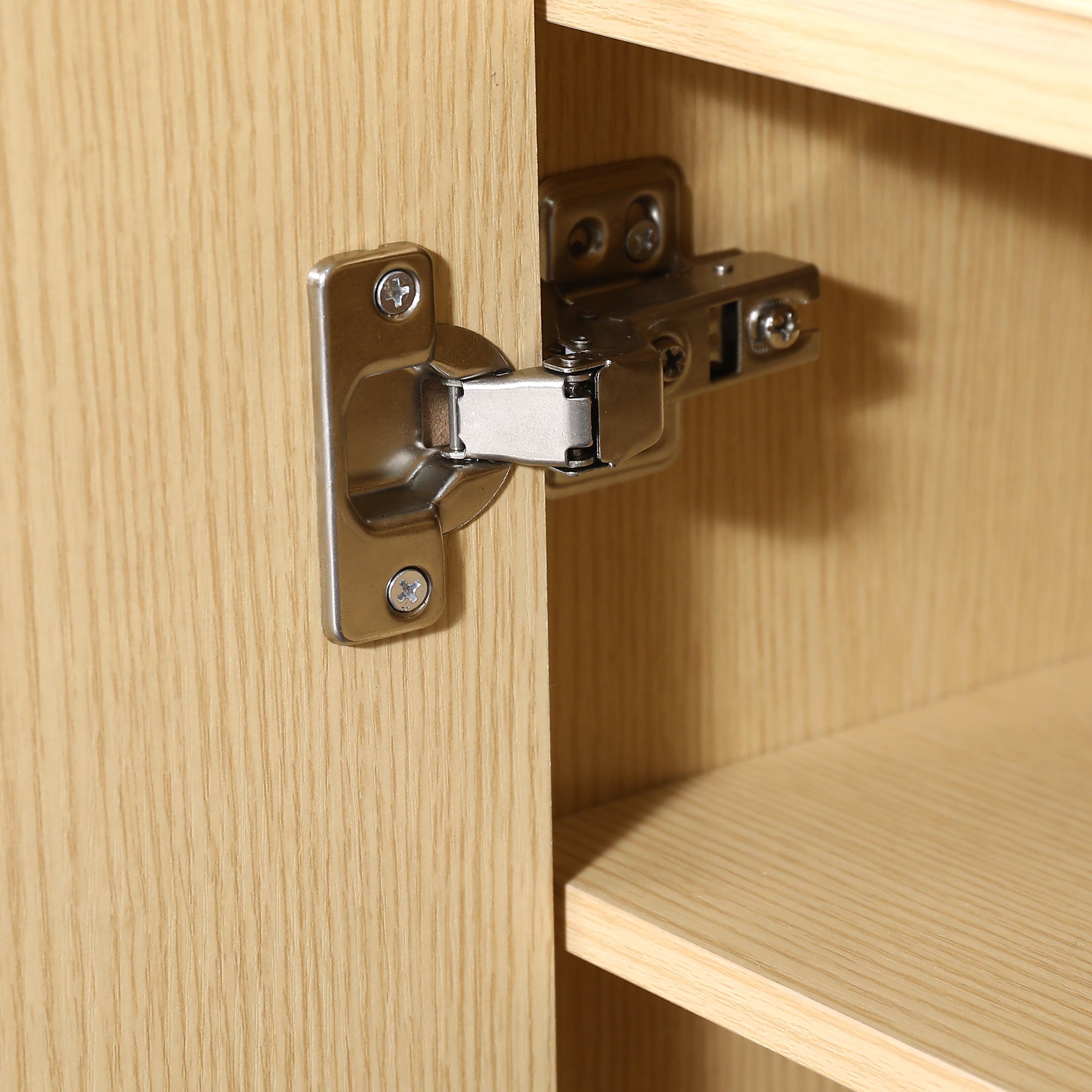 Close-up of a silver metal cabinet hinge installed on a light wood door and frame
