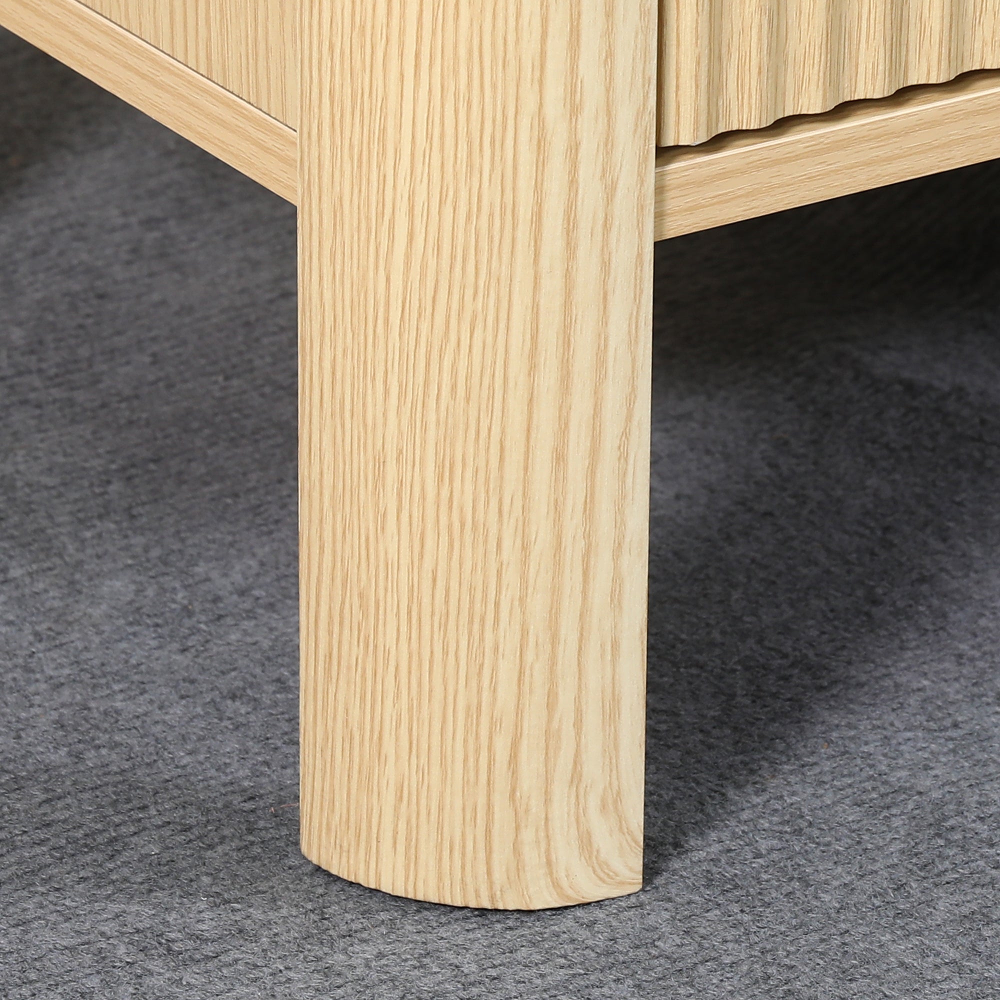 Close-up of a light-colored natural oak wood furniture leg on a grey carpet.