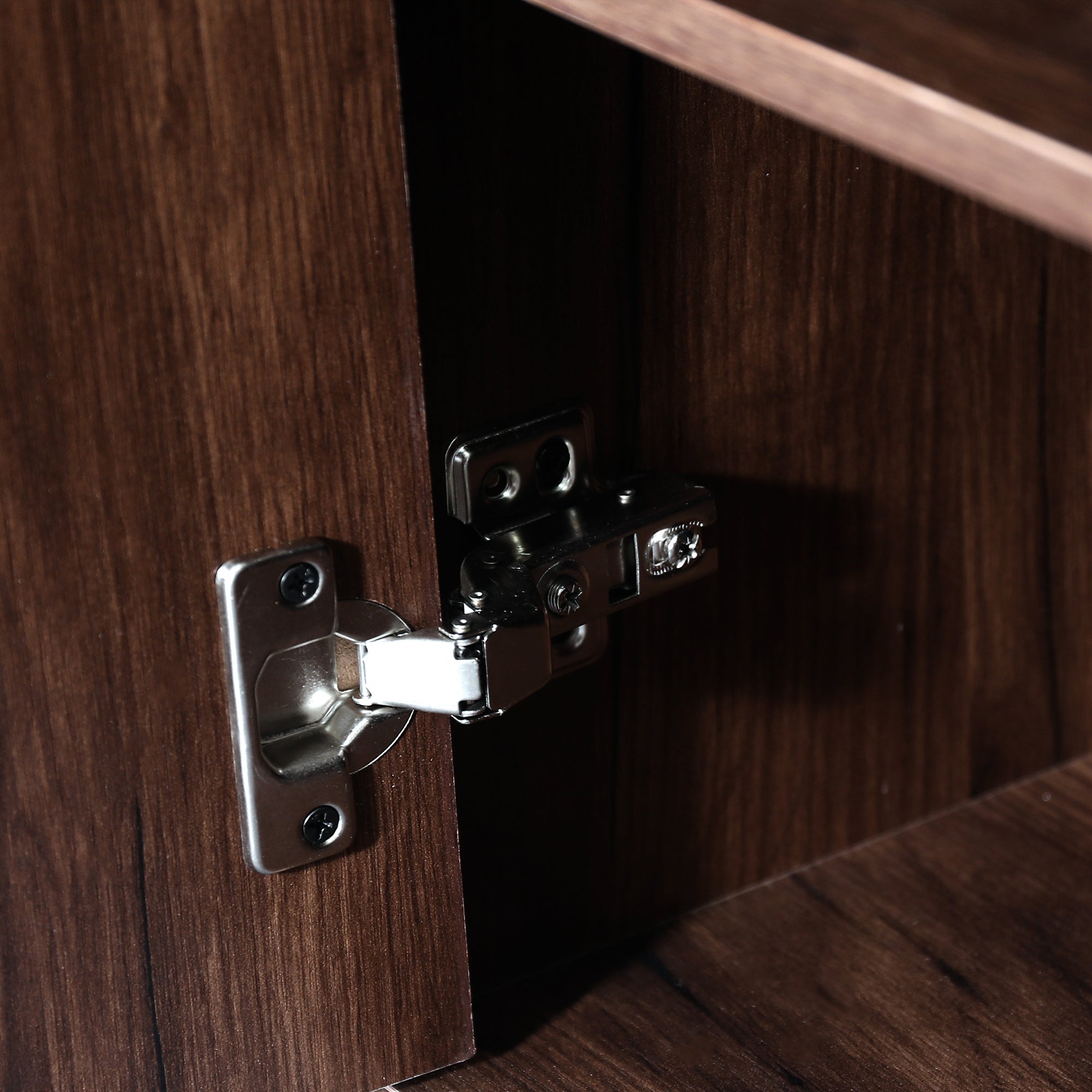 Close-up of a silver metal cabinet hinge installed on dark wood furniture.