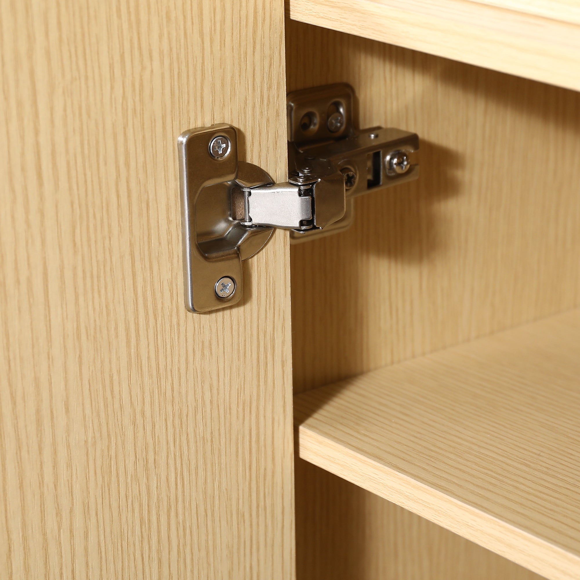 Close-up of a silver metal cabinet hinge installed on a light wood cabinet door.