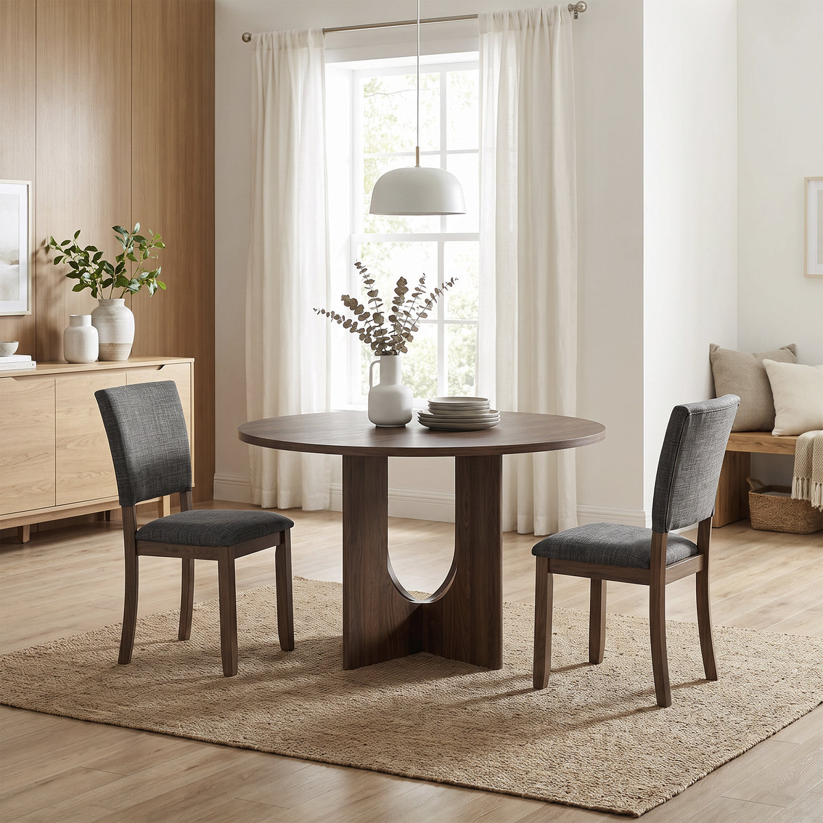 Round dark wood dining table with two grey upholstered chairs on a jute rug